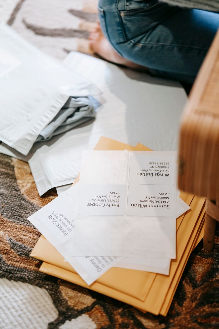 High angle of anonymous woman near envelope parcels for shipment with papers with addresses on carpet on floor near table in light home